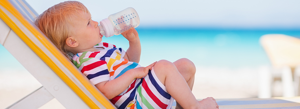 bébé qui boit un biberon sur un transat à la plage